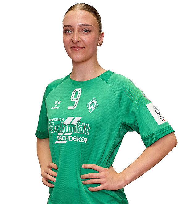 Eine junge Frau im grünen Sport-Shirt mit der Nummer 9 drauf, sie stemmt die Arme in die Hüften und lächelt.