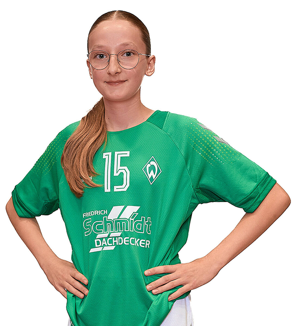 Eine junge Frau im grünen Sport-Shirt mit der Nummer 15 drauf, sie stemmt die Arme in die Hüften und lächelt.