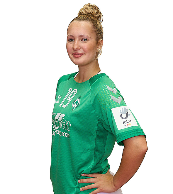 Eine junge Frau im grünen Sport-Shirt mit der Nummer 19 drauf, sie stemmt die Arme in die Hüften und lächelt.