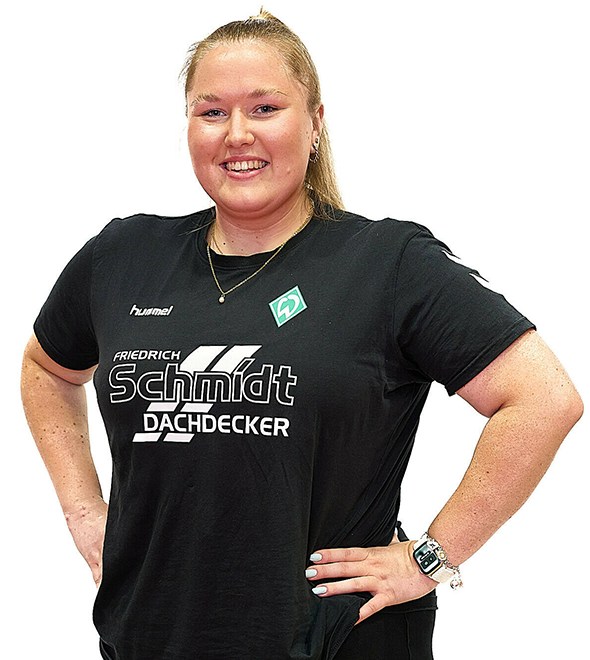 Eine Frau im schwarzen Sport-Shirt, sie stemmt die Arme in die Hüften und lächelt.