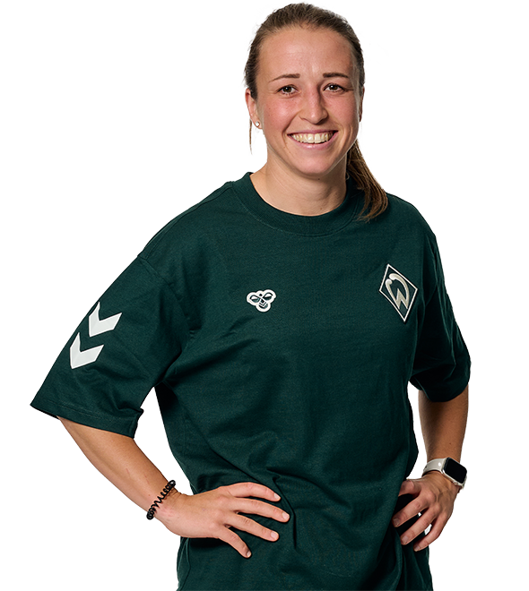 Smiling person wearing a dark green sports shirt with logos, hands on hips, against a plain background.