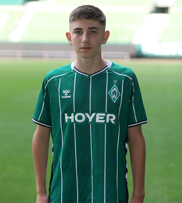 Portrait von Justin Eva. Er stemmt die Hände in die Hüften.