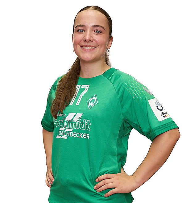 Eine junge Frau im grünen Sport-Shirt mit der Nummer 17 drauf, sie stemmt die Arme in die Hüften und lächelt.