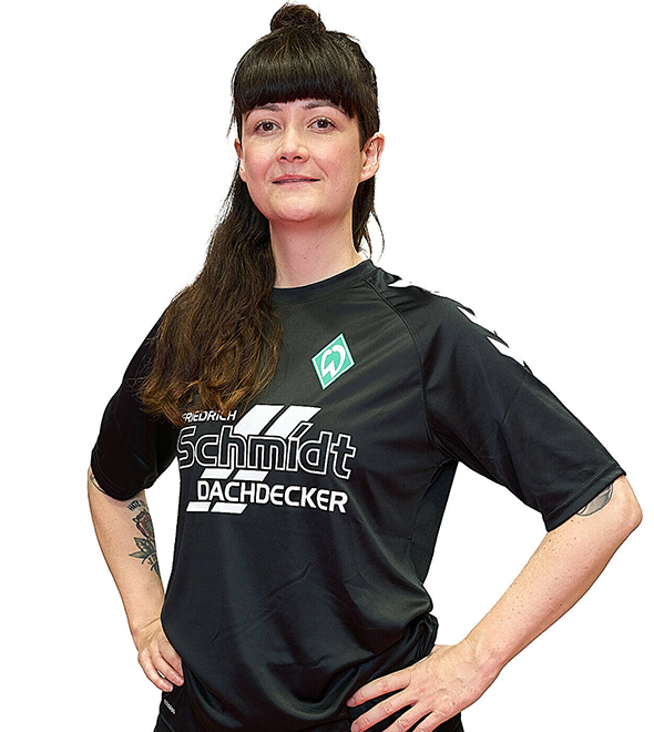 Eine Frau im schwarzen Sport-Shirt, sie stemmt die Arme in die Hüften und lächelt.