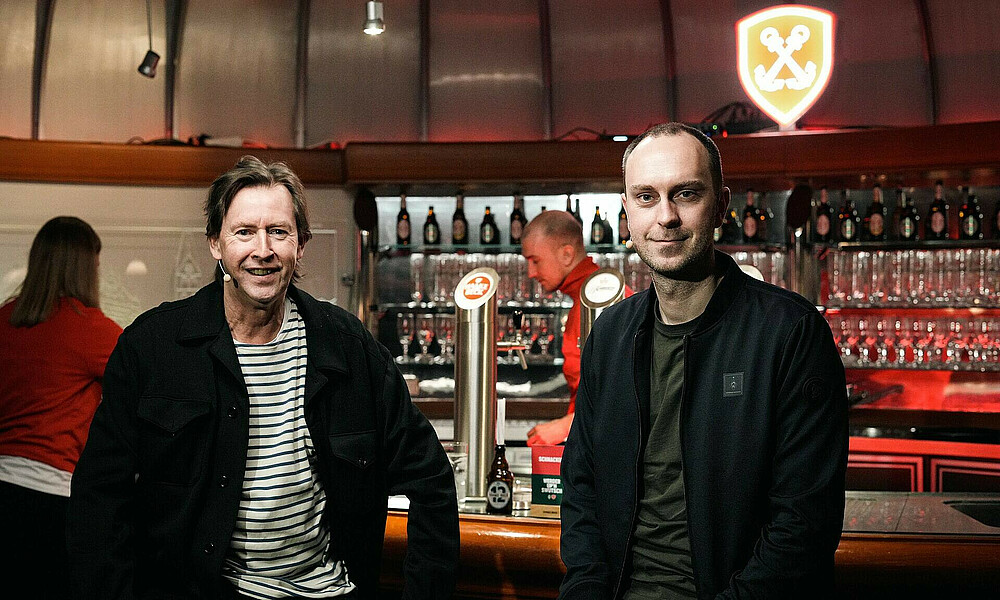 Moderator Lou Richter und Ole Werner mit Blick in die Kamera. 