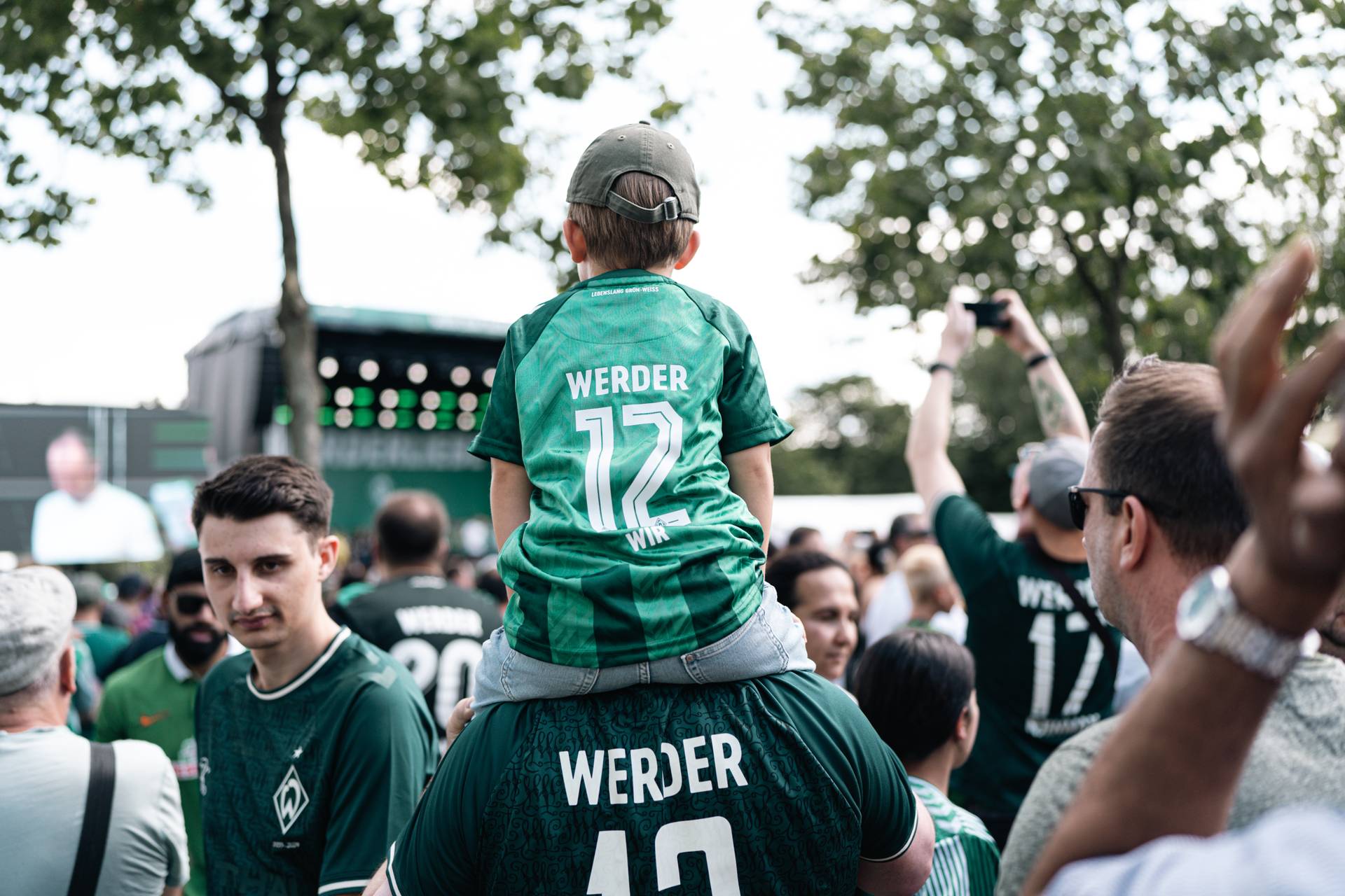 Ein kleines Kind sitzt im Werder-Trikot auf den Schulter seines Vaters.