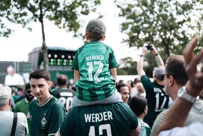 Ein kleines Kind sitzt im Werder-Trikot auf den Schulter seines Vaters.