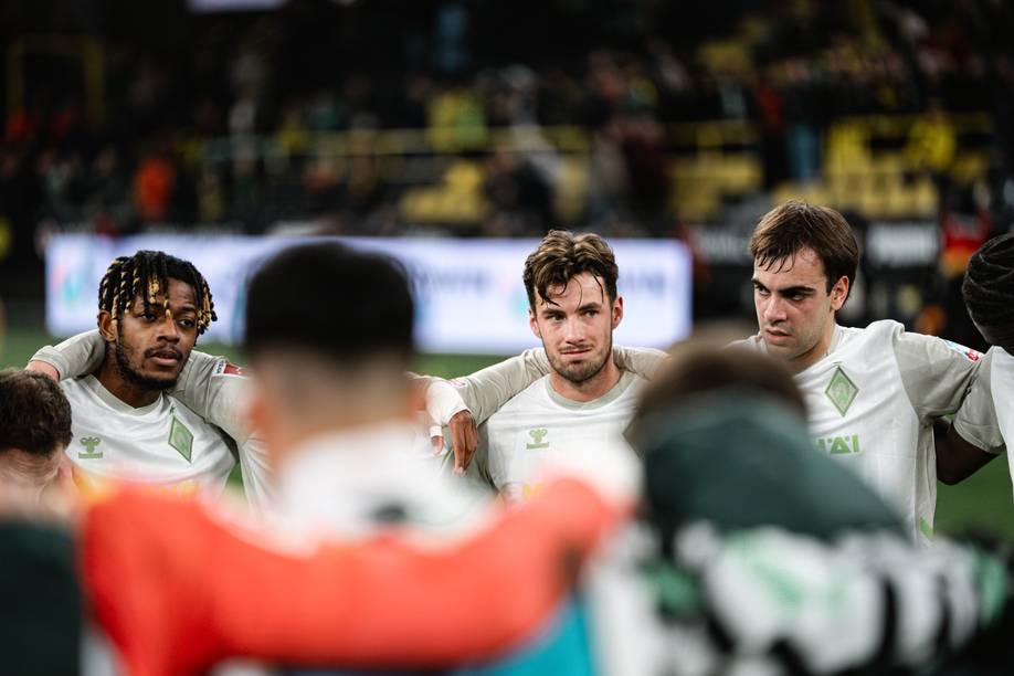 Blick über die Schultern einiger Spieler in den Mannschaftskreis. Zu sehen sind von links nach rechts Samuel Mbangula, Olivier Deman und Jovan Milosevic.