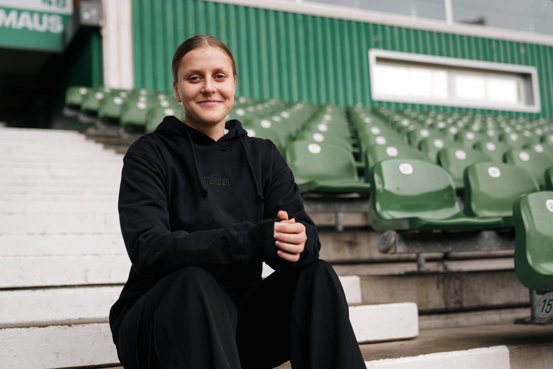 Sarah Gutmann sitzt auf den Treppen im Weserstadion, im Hintergrund sind leere Sitzschalen zu sehen.