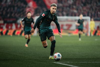 Justin Njinmah läuft im dunkelgrünen Third-Trikot mit dem Ball am Fuß im Stadion.