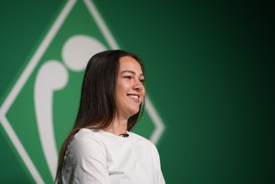Maja Sternad in einem weißen Hemd. Grüner Hintergrund mit einem weißen, abstrakten Logo.