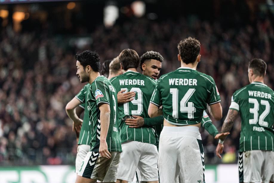 Justin Njinmah ugs Jovan Milošević. More Werder players stand around them.
