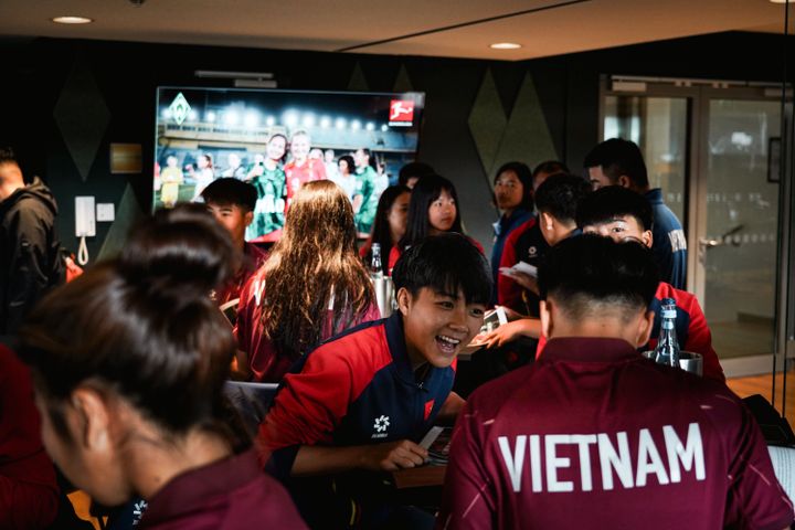 Eine Gruppe junger Leute in einheitlichen roten Jacken mit der Aufschrift „Vietnam“ auf dem Rücken versammelte sich in einem Raum, einige lächelten und unterhielten sich.