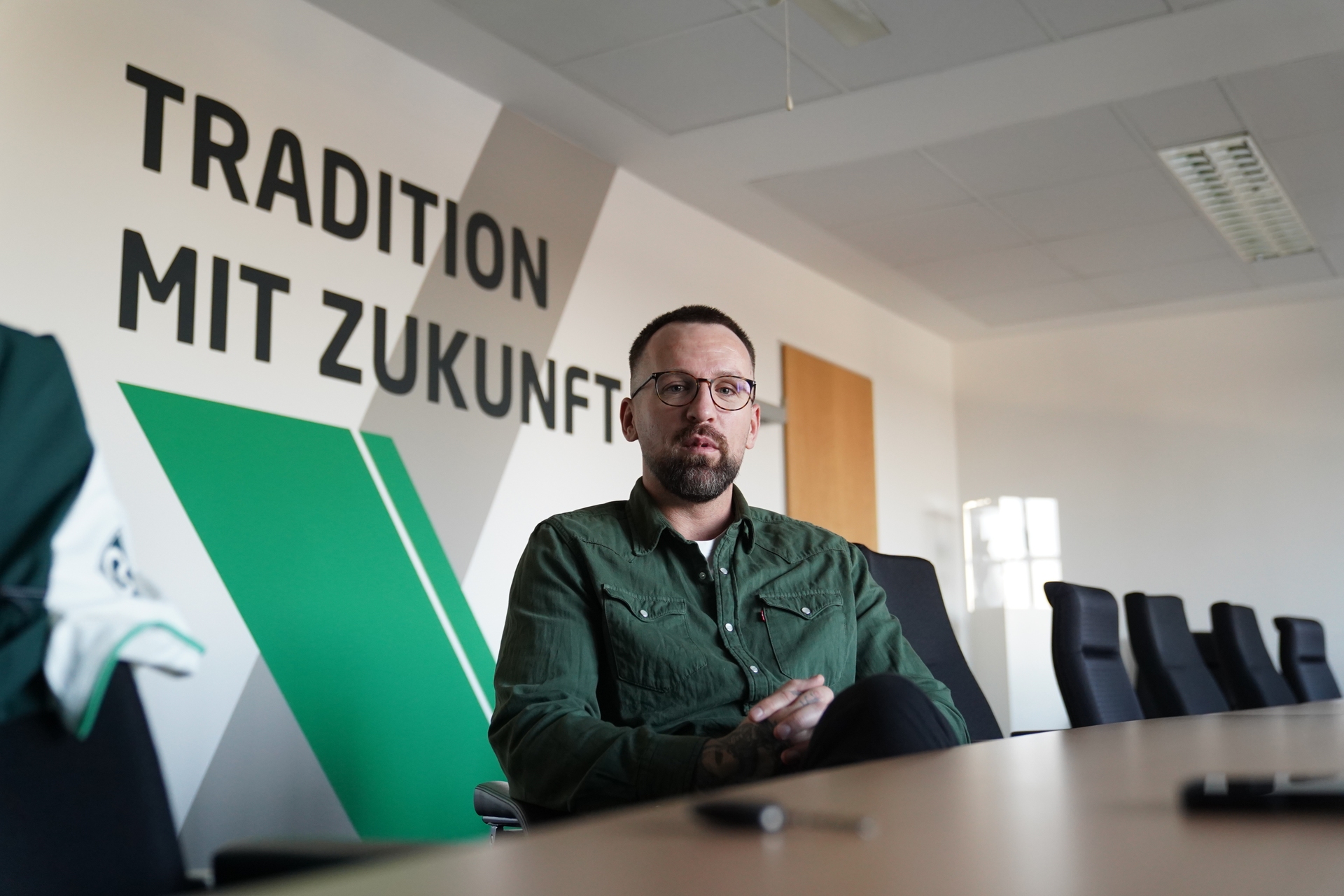 Edgar Kary sitzt vor einer grün-weißen Wand und spricht in die Kamera.