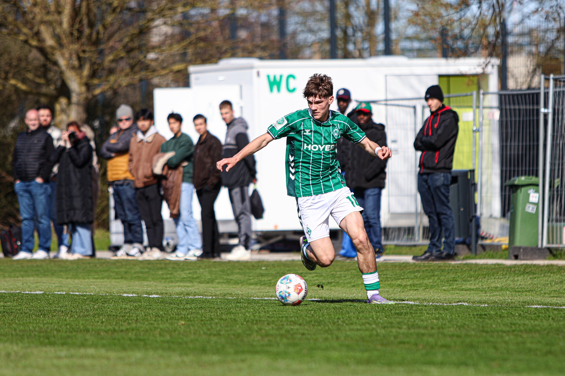 Ein Spieler der U17 im grünen Trikot läuft und treibt den Ball vor sich.