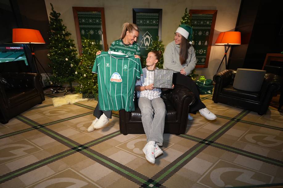 Medina Desic hält das Heimtrikot in den Händen, das Werder-Logo ist im Tannenbaum-Design. Neben ihr sitzen Michelle Ulbrich, die ein Geschenk in den Händen hält, und Mariella El Sherif mit einer Weihnachtsmütze auf einem Sessel.
