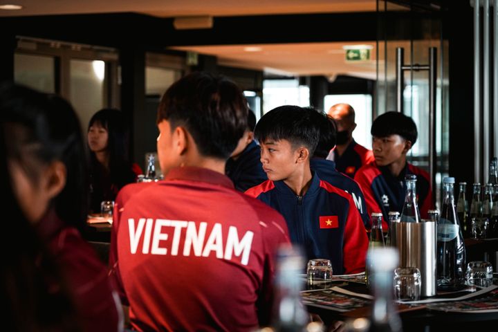 Menschen in passenden Vietnam-Sportjacken sitzen in einem schwach beleuchteten Raum mit gedeckten Tischen.