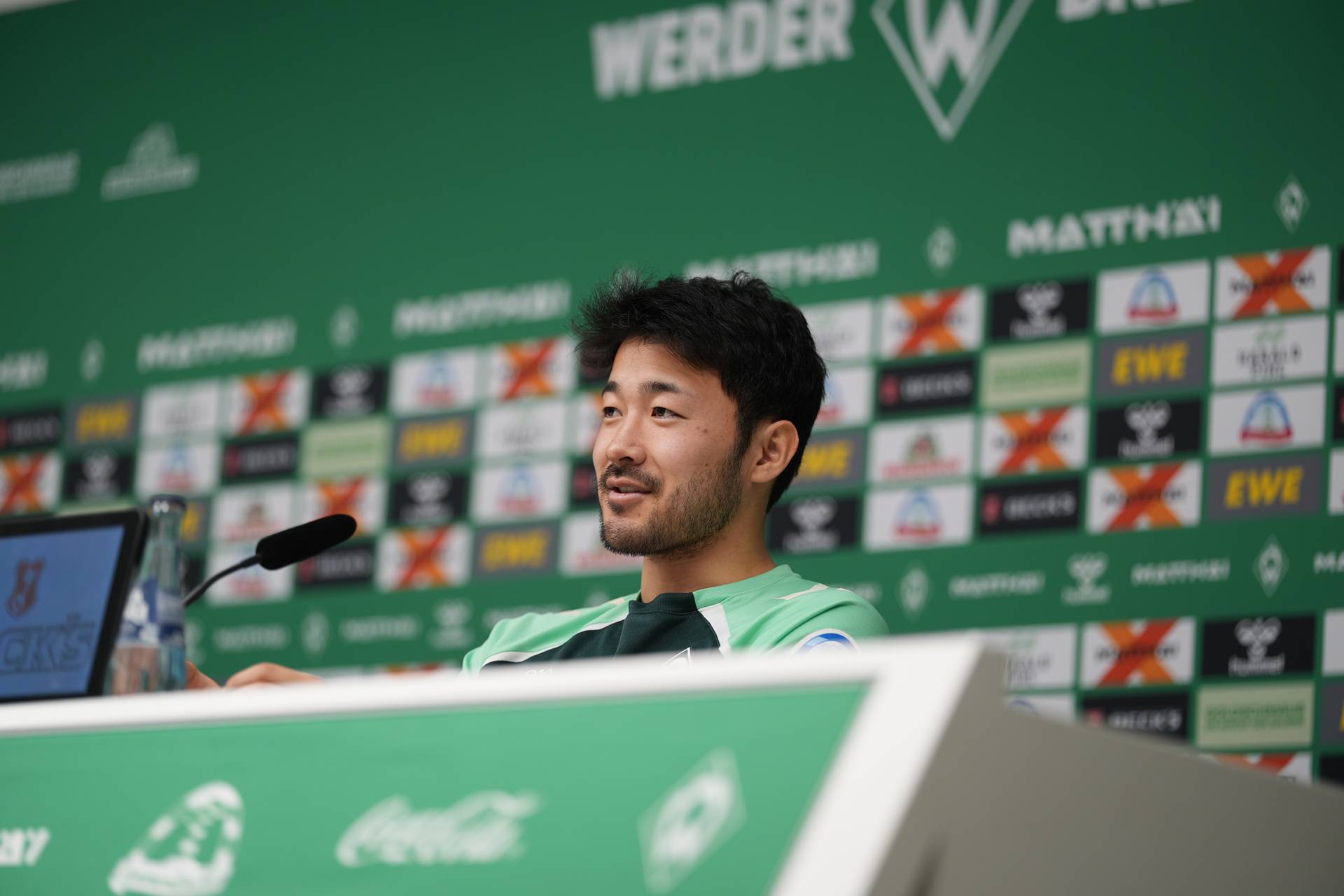 Yukinari Sugawara spricht ins Mikro auf der PK-Bühne.