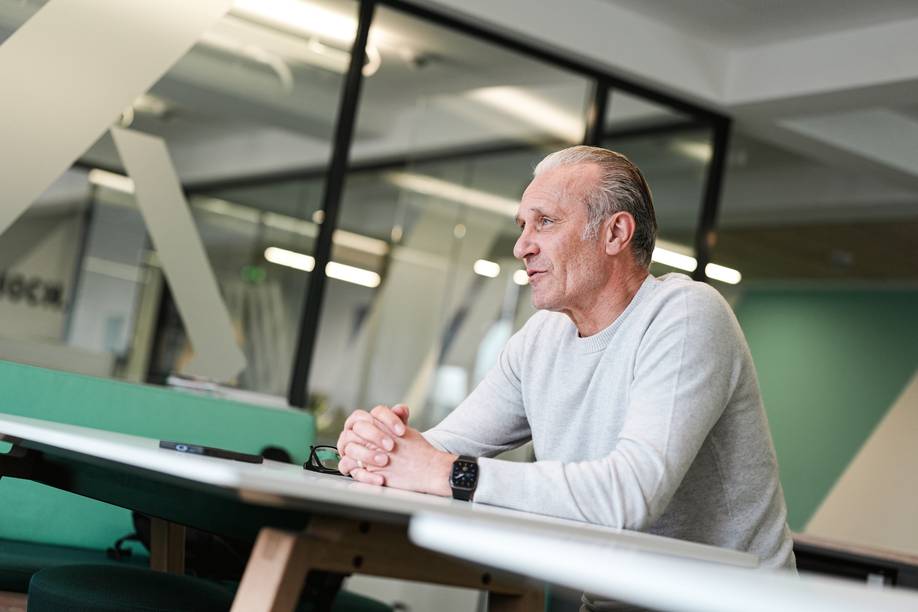 Thomas Wolter sitzt in einem grauen Pullover an einem Tisch und faltet seine Hände ineinander.