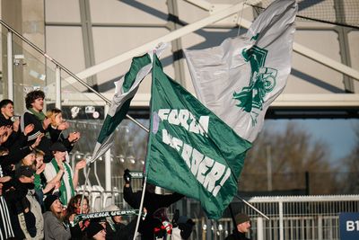 Fans jubeln begeistert und schwenken große grün-weiße Fahnen mit Aufschrift in einem Stadion.