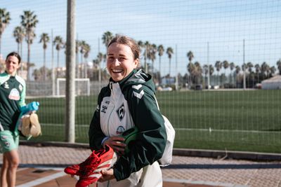 Michaela Specht im Trainingslager in Spanien hält Fußballschuhe in der Hand und lacht.