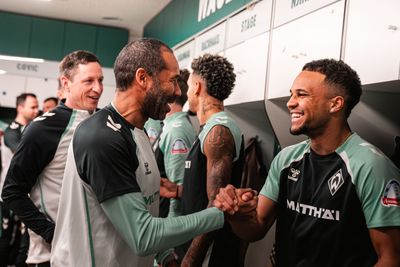 Daniel Thioune und Felix Agu klatschen in der Kabine ab. Beide lächeln sich an.