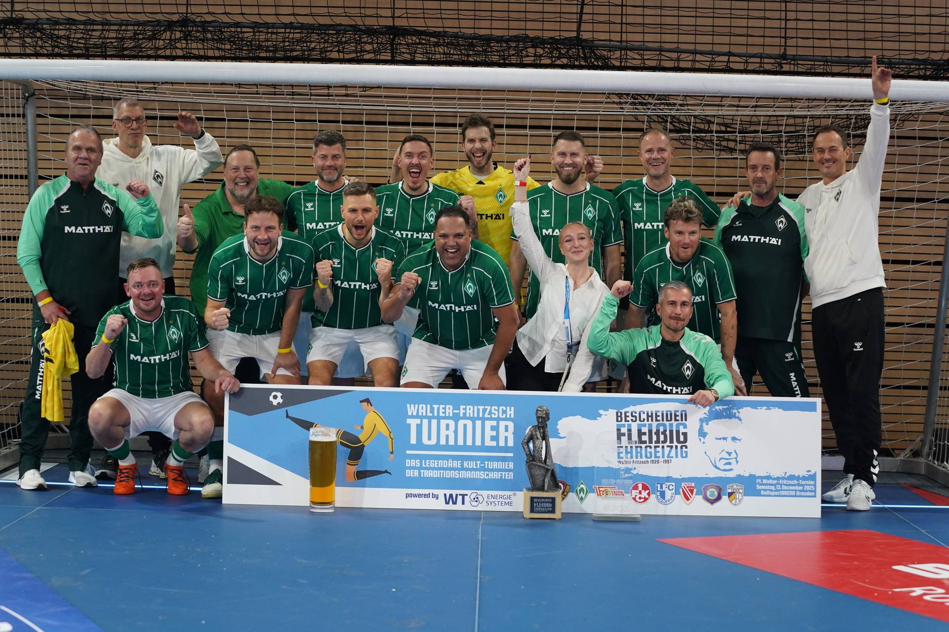 Die WERDER LEGENDEN jubeln im Tor mit einer Werbebande und dem Pokal.