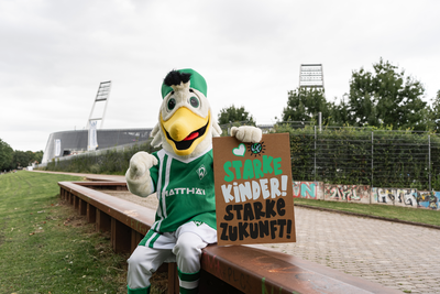 Möwe Toni hält ein Schild aus Pappe mit der Aufschrift "Starke Kinder, Starke Zukunft!"