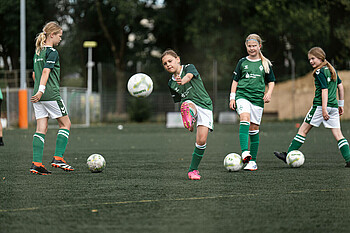 Ein Mädchen schießt beim MÄDCHEN CAMP gegen den Ball. Andere Mädchen stehen drumherum.