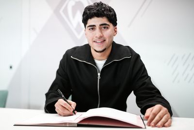 Darwin Soylu sitzt mit einem Stift in der Hand und einem Vertrag vor sich liegend an einem Tisch.