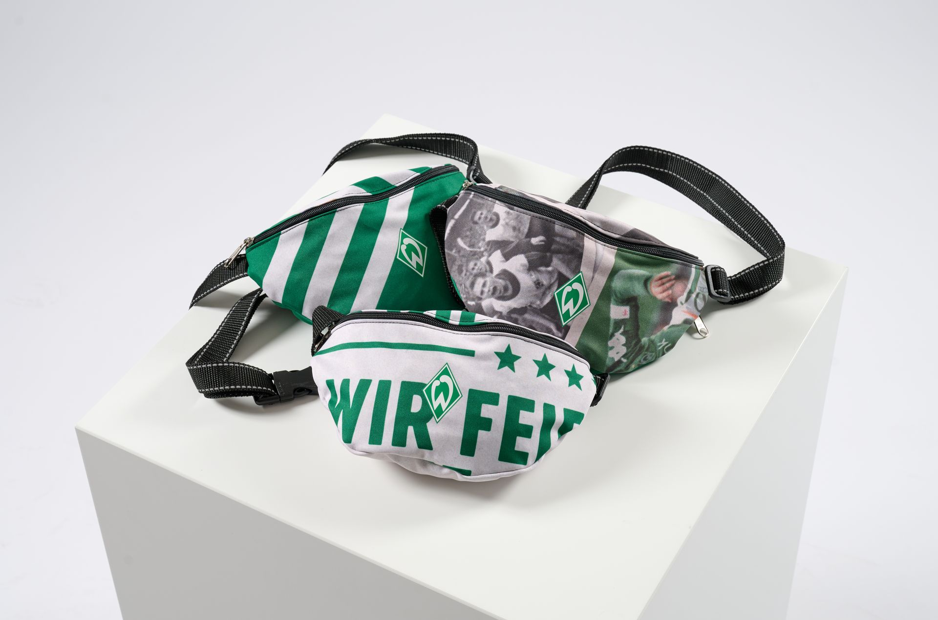 Drei grün-weiße Gürteltaschen mit sportlichen Motiven, Streifen und Schriftzügen, präsentiert auf weißem Hintergrund.