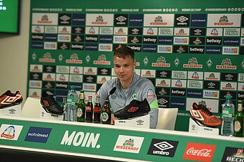 Niklas Schmidt sitzt lächelnd auf dem Podium vor den Mikrofonen.