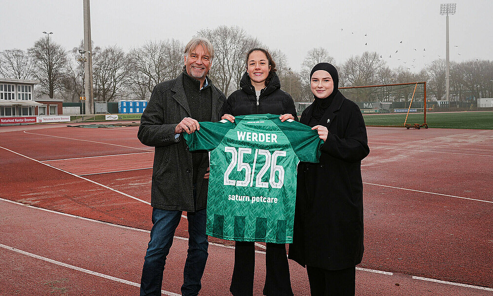 null Drei Personen halten gemeinsam ein Werder-Trikot mit