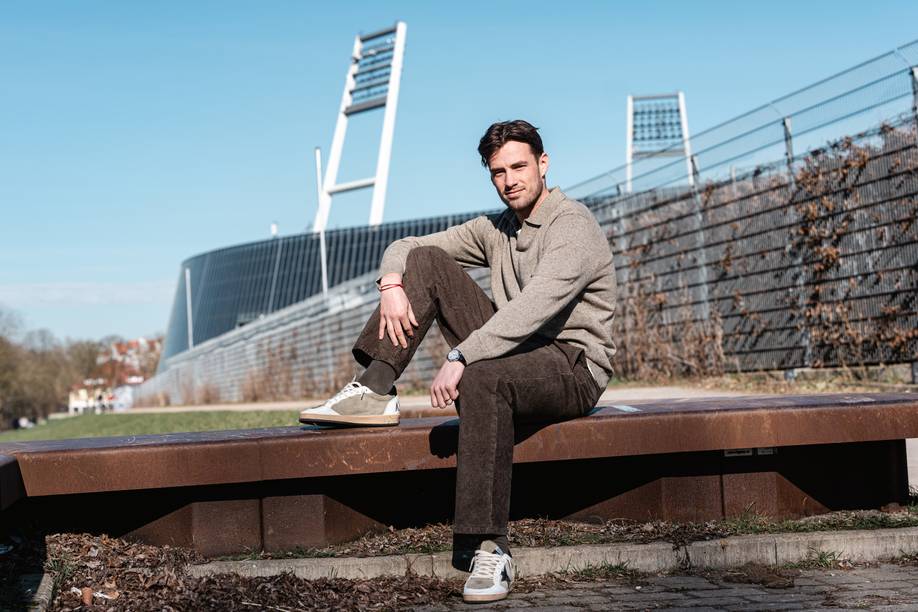 Olivier Deman sitzt auf einer Bank, im Hintergrund sind die Flutlichtmasten des Weserstadions zu sehen.