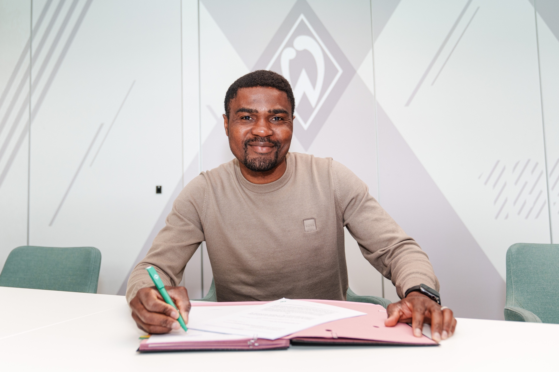 Cédric Makiadi sitzt an einem Tisch und unterschreibt einen Vertrag, wobei er in die Kamer schaut.