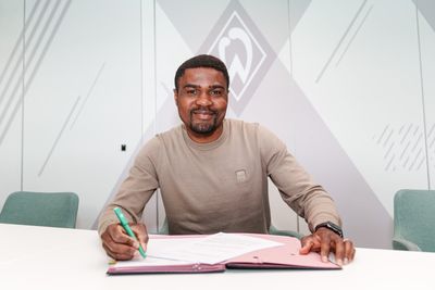 Cédric Makiadi sitzt an einem Tisch und unterschreibt einen Vertrag, wobei er in die Kamer schaut.