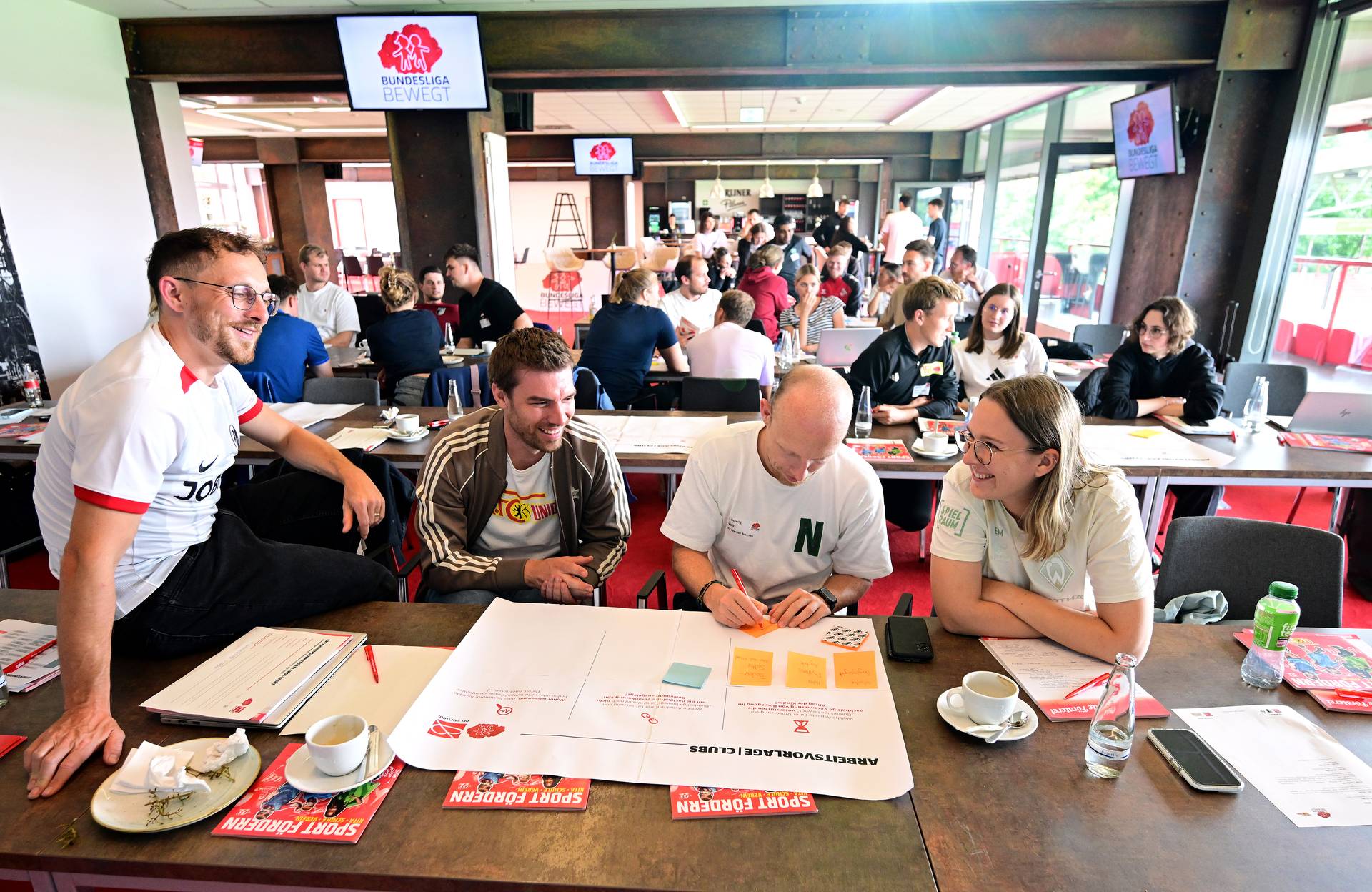 Menschen sitzen in einem geschäftigen Konferenzraum um einen Tisch herum und diskutieren während eines Workshops über Dokumente.