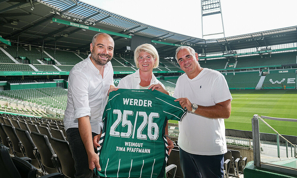 null Drei Personen präsentieren ein Werder Trikot mit Weingut Pfaffmann Flock im Stadon.