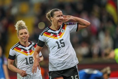 Zwei Fußballspielerinnen in deutschen Trikots feiern auf dem Spielfeld. Die Spielerin vorne macht eine Geste mit ihrer Hand in der Nähe ihres Ohrs.