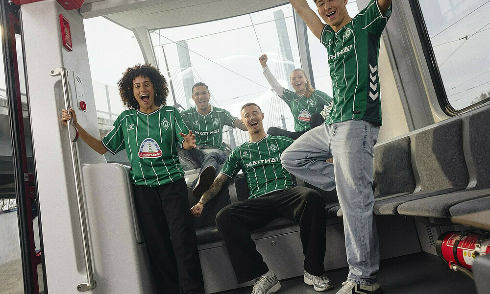 Spielerinnen und Spieler in einer Straßenbahn mit dem neuen Trikot. 
