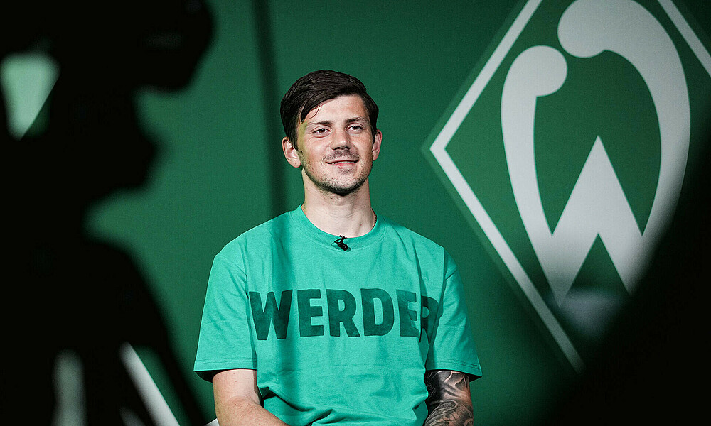 null Dawid Kownacki sitzt beim Interview, links im Vordergrund eine Videokamera. Hinten die Werder-Raute.