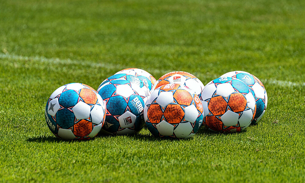 Bälle liegen auf dem Rasen eines Fußballplatzes.