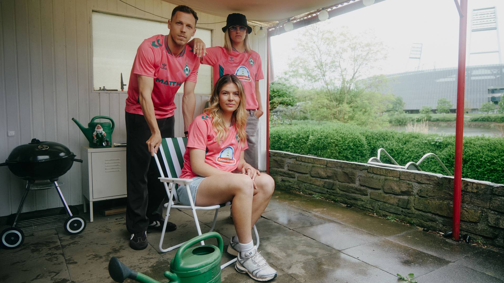 Three Werder players standing on a patio wearing the new coral-coloured Werder third kit