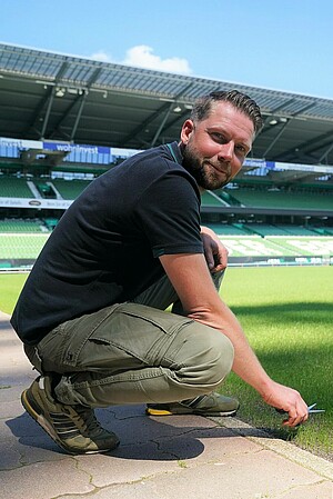 null Greenkeeper Tim Engelke schneidet den Rasen mit einer kleinen Schere.