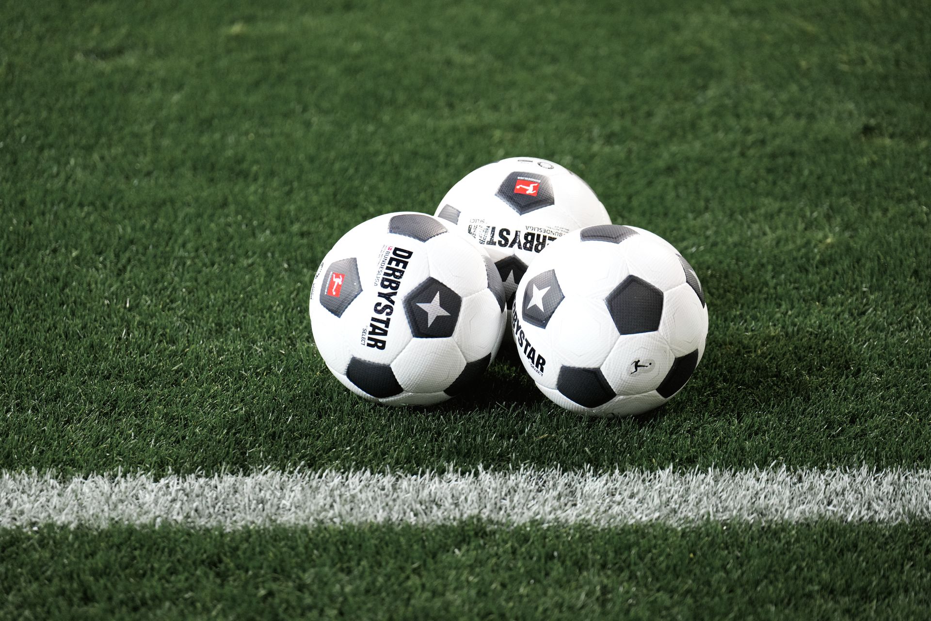 Drei schwarz-weiße Fußbälle auf einem grünen Rasenfeld in der Nähe einer weißen Linie.