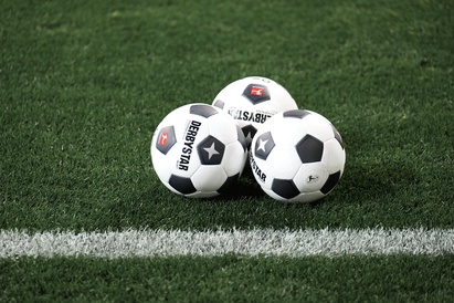 Drei schwarz-weiße Fußbälle auf einem grünen Rasenfeld in der Nähe einer weißen Linie.