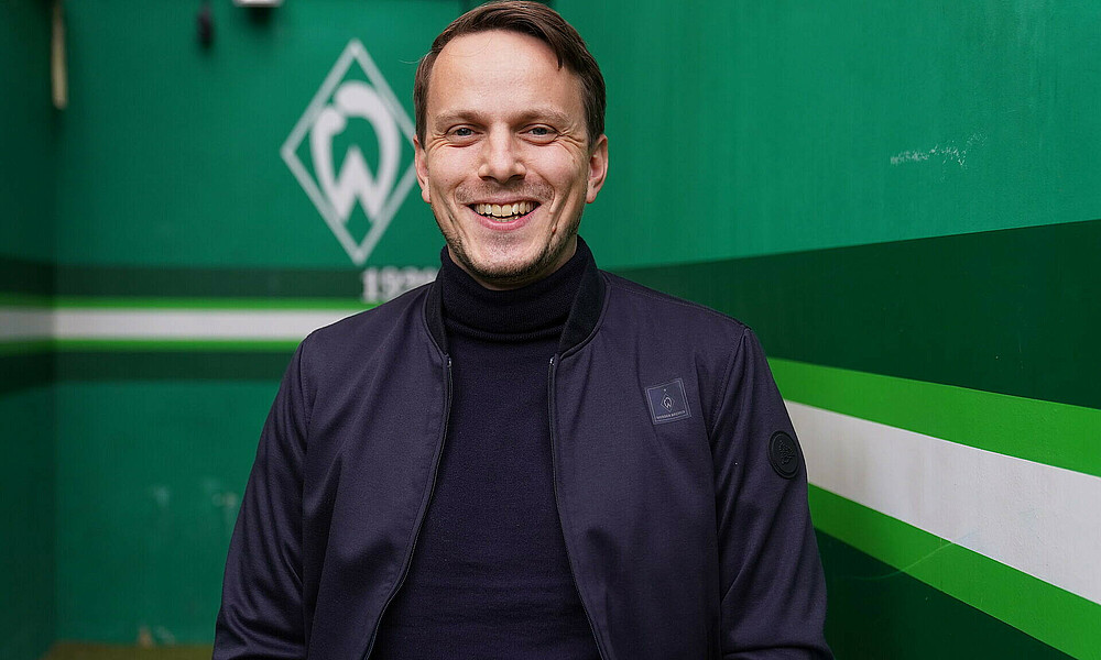 Dr. Henning Hofmann steht vor der Werder-Raute und lächelt in die Kamera