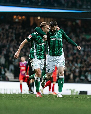 Marco Grüll und Oliver Burke jubeln zusammen im Werder-Heimtrikot auf dem Platz des Weserstadions