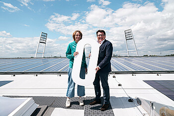 CSR-Direktorin Anne-Kathrin Laufmann und Werder-Präsident Hubertus Hess-Hrunewald auf dem Stadiondach mit einer großen weißen Null in der Hand.