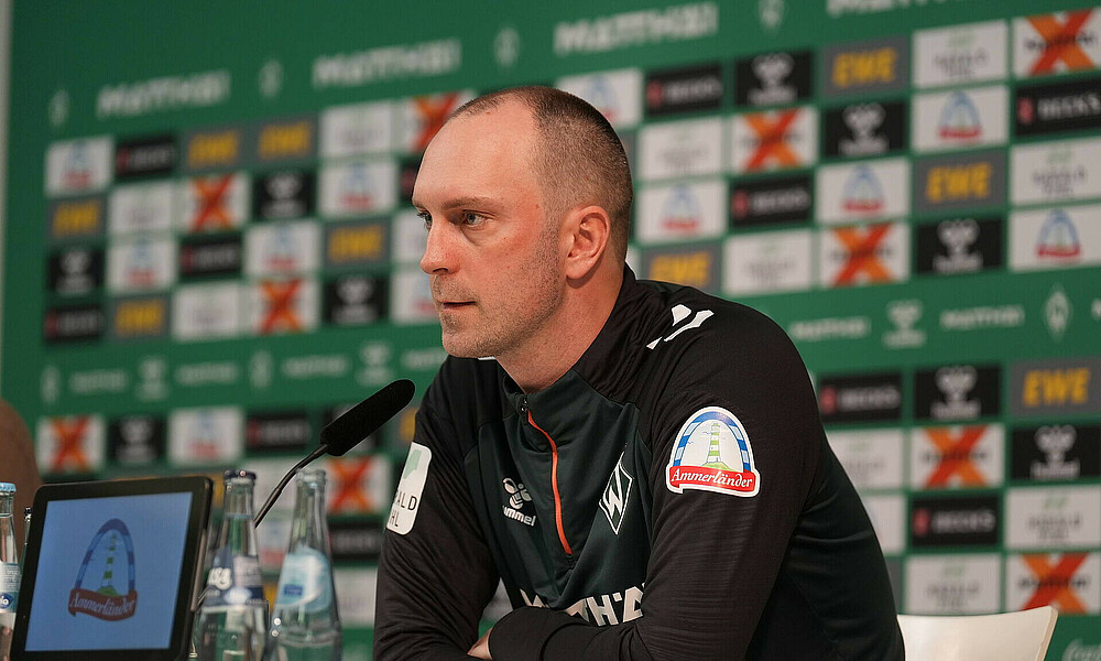 Werder-Cheftrainer Ole Werner guckt zur Seite auf dem Podium bei der Pressekonferenz